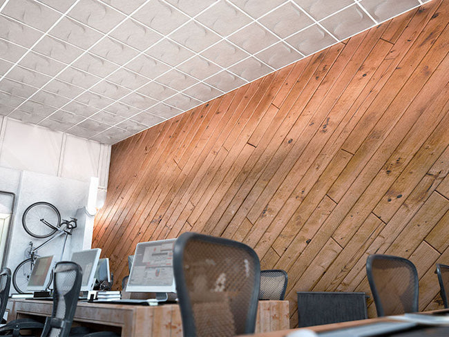 Modern office ceiling design featuring textured, white drop ceiling tiles above a workspace with a unique wooden accent wall