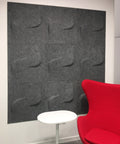 Twist FeltForms 2' x 2' Acoustic wall tile in mottled grey inside a phone booth with comfy red chair and side table.